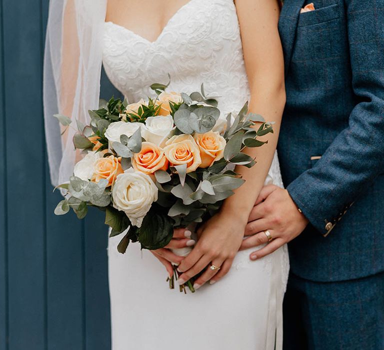 Bride holds her white and peach floral bouquet complete with green foliage