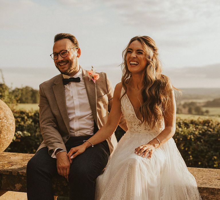 Bride & groom sit with one another on balcony outdoors as the sun shines