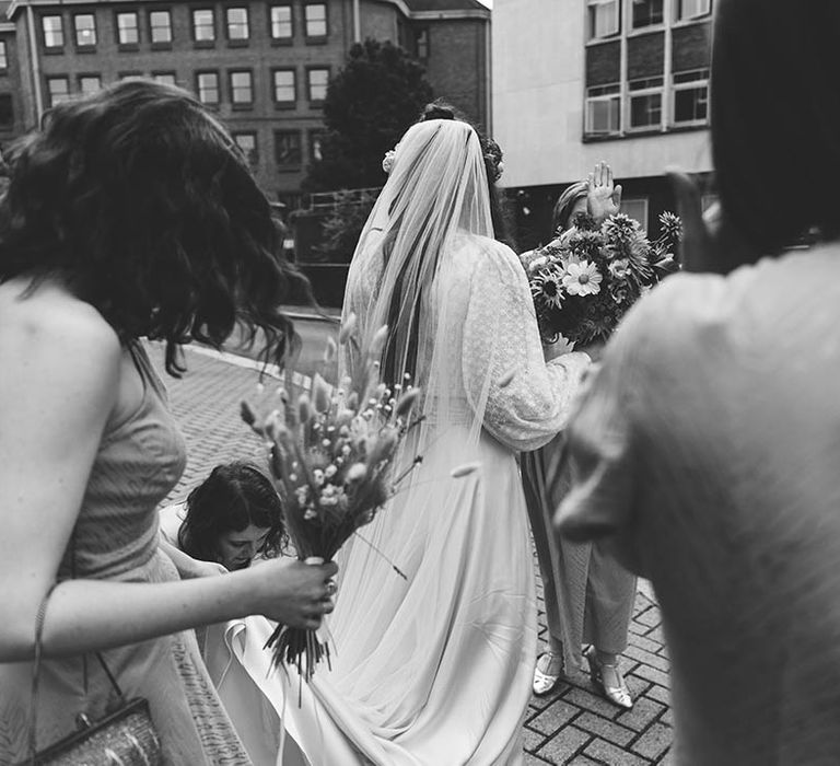 Black & white image of bride walking and holding floral bouquet