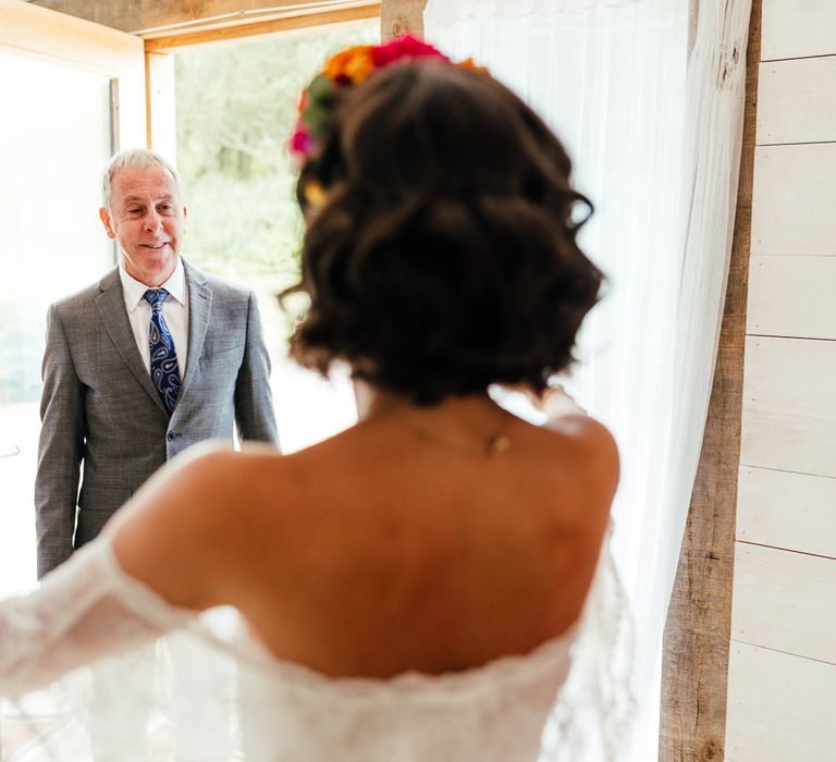 Bride in lace off the shoulder wedding dress and flower crown greens father in grey suit before outdoor wedding ceremony