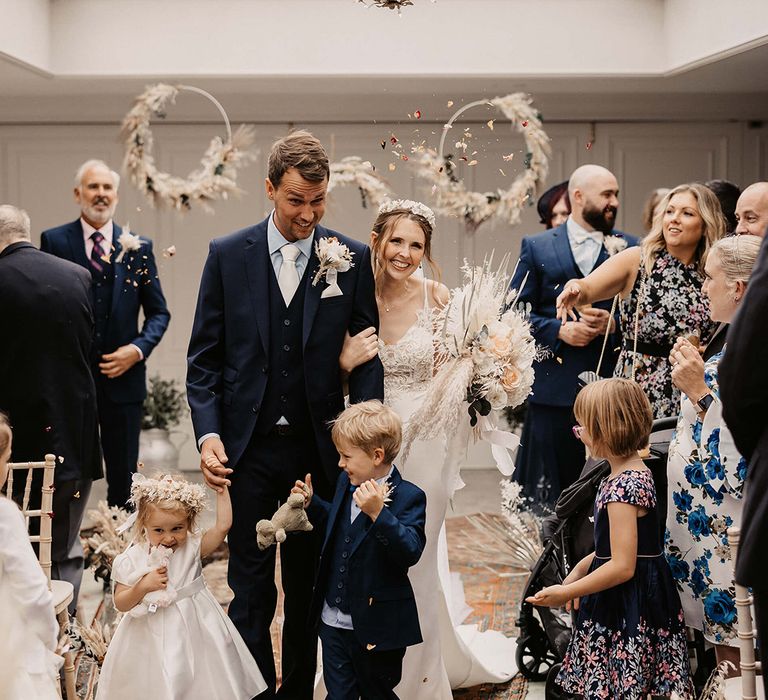 Family walk down the aisle after wedding ceremony as guests throw confetti around them