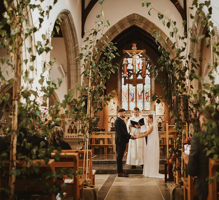 Trees lining the church wedding ceremony aisle with bride and groom exchanging vows at the altar 