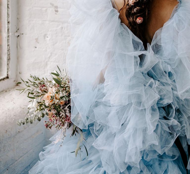 Blue layered tulle coloured wedding dress and braided plait wedding hairstyle with pink dry flower hair accessories 