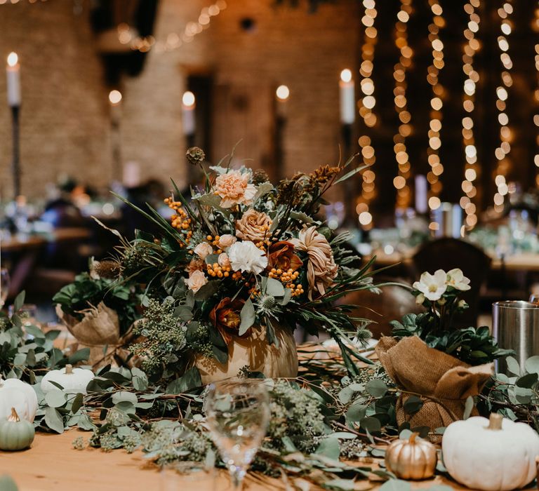 Green and orange floral centrepiece with white and gold pumpkins for autumnal rustic wedding reception