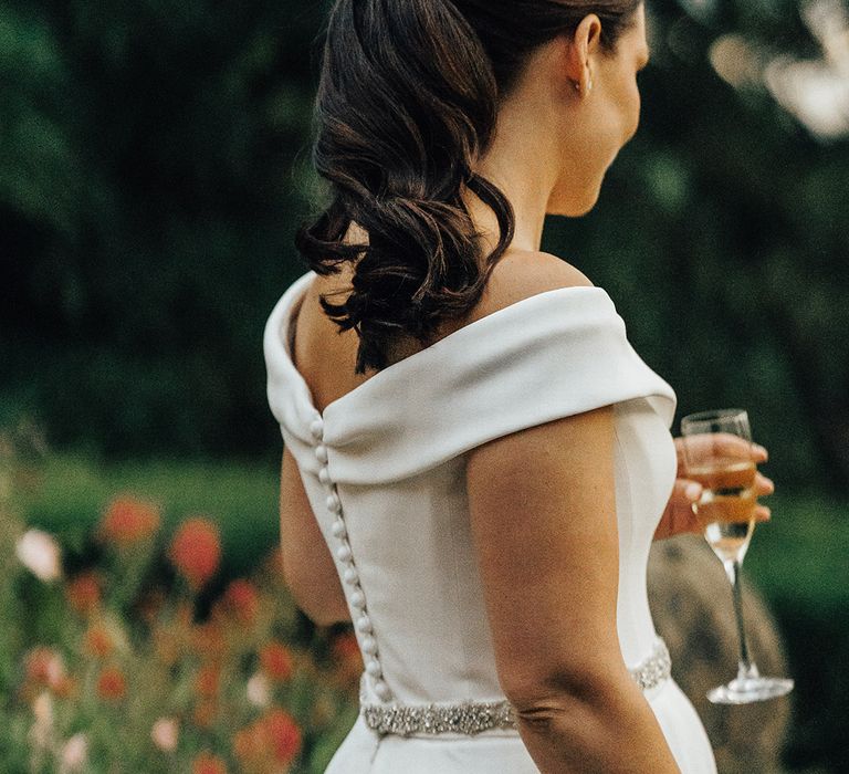 Bride with an elegant wavy ponytail in a Suzanne Neville wedding dress with diamanté waist detail and buttons down the back 