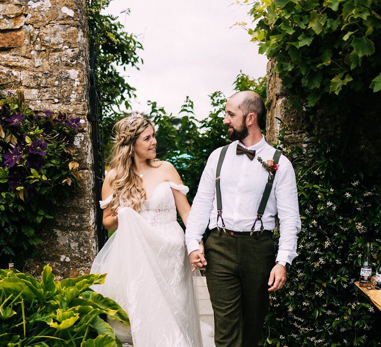 Bride strolls with groom in a forest green trouser and white shirt with matching braces