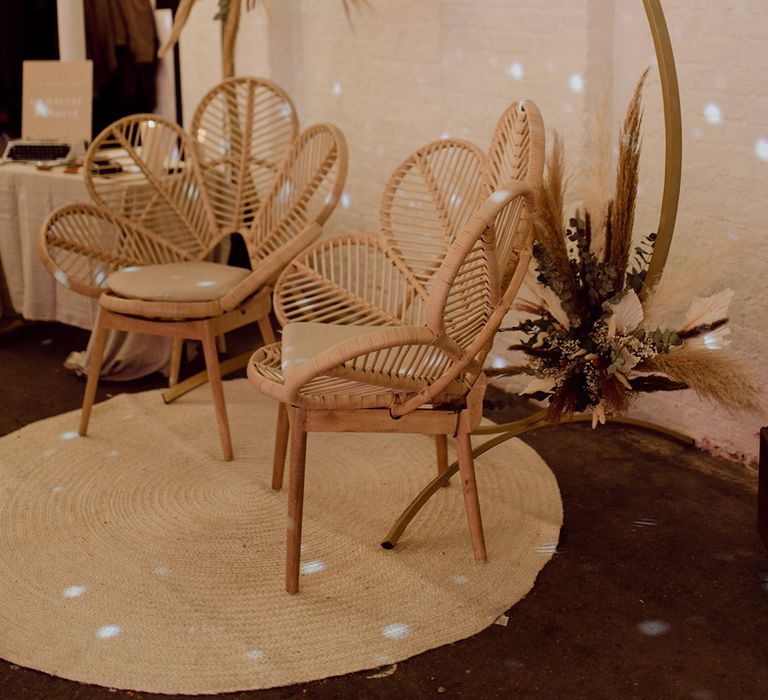 Wooden flower rattan chairs on circular white rug in front of moongate with dried flower details at industrial venue in Brixton