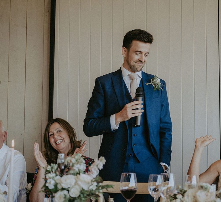 Groom in three-piece blue suit gives a speech at his wedding in Primrose Hill