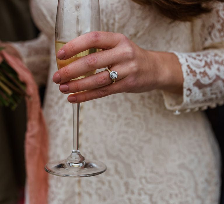 Bride's brilliant round wedding ring holding glass of champagne in lace wedding dress 