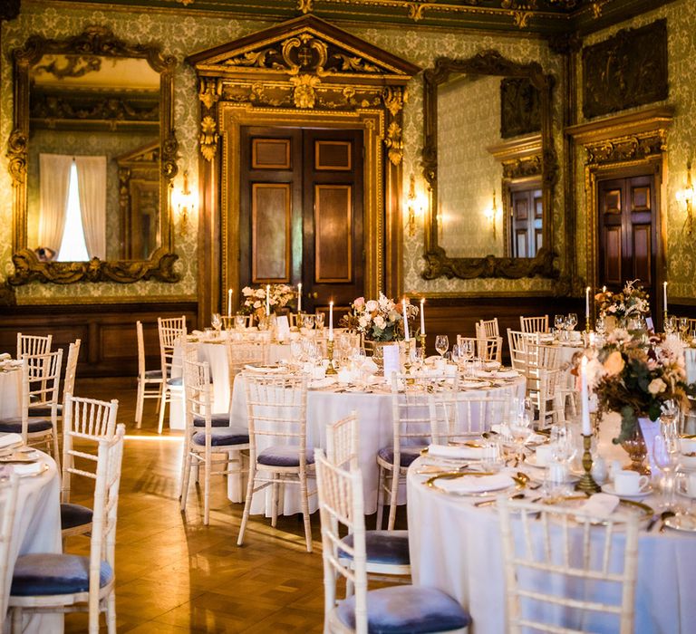 Crystal chandelier and grand gold wedding reception room with white and gold table setting with roses as centrepiece at Hawkstone Hall