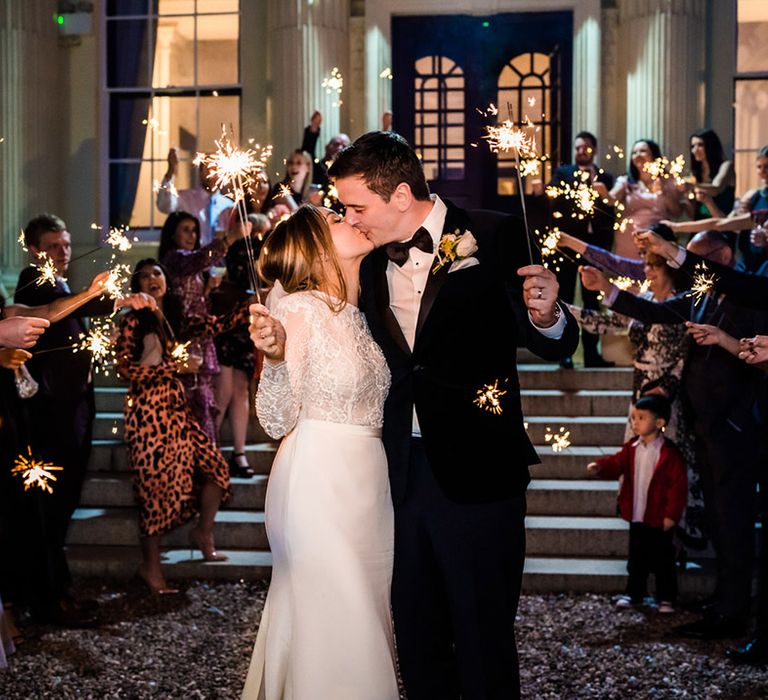 Bride and groom share a kiss while everyone waves a sparkler 