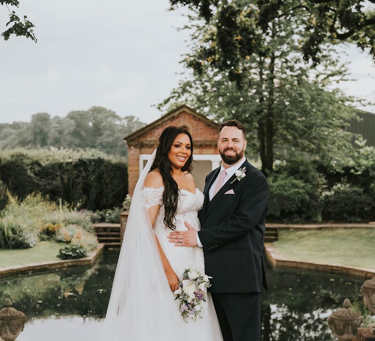 Groom holds the bride who wears a stunning lace detailed long veil at Micklefield Hall