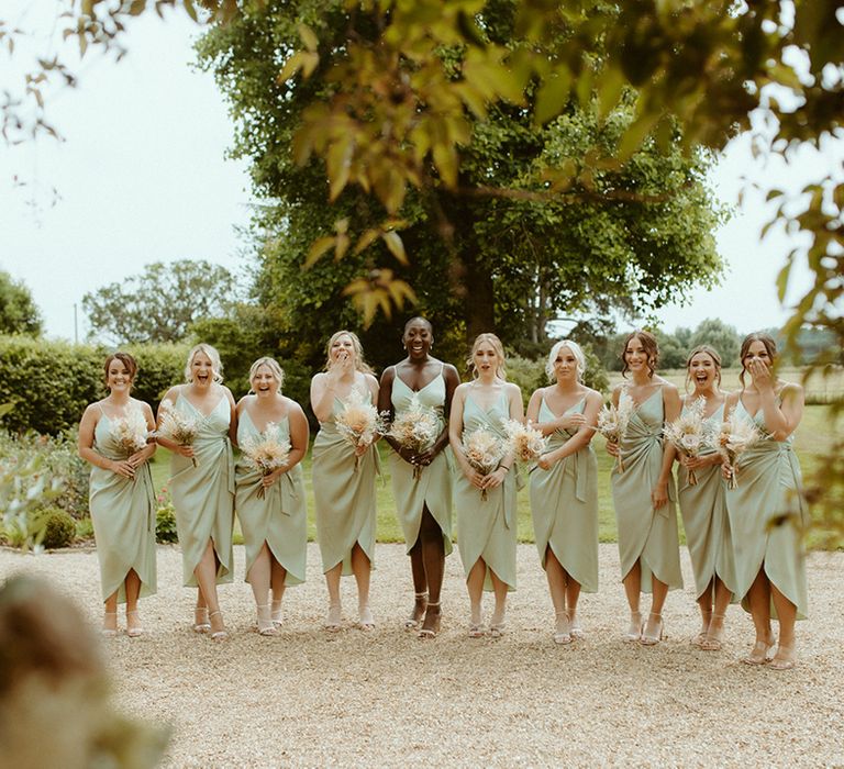 Bridesmaids in sage green satin wrap dresses get their first look at the bride