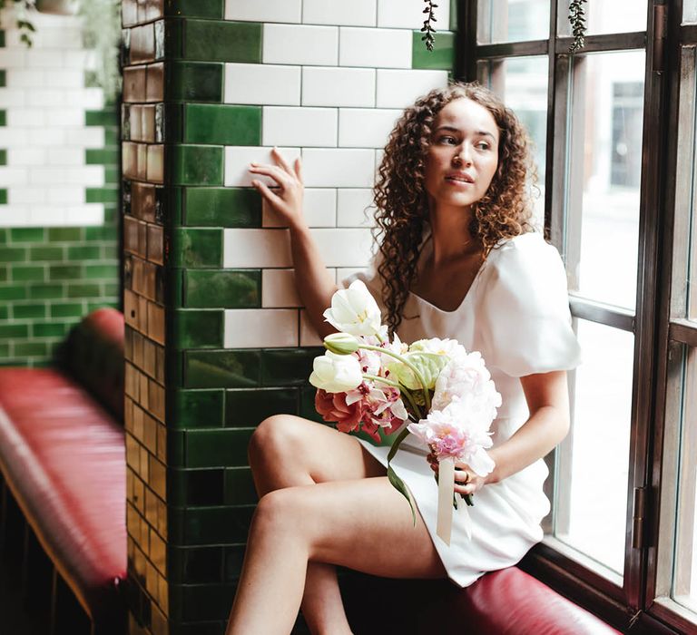 Bride in a short wedding dress and green scrappy sandals holding a white tulip and pink peony bouquet at Singer Tavern urban wedding venue 