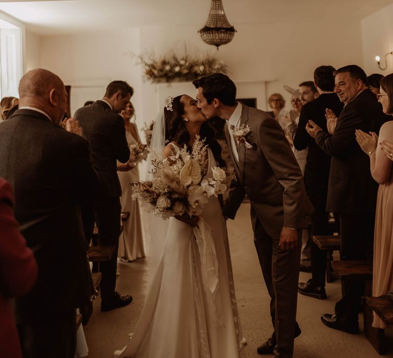 Bride and groom share a kiss as they walk back down the aisle as a married couple at their boho luxe wedding 