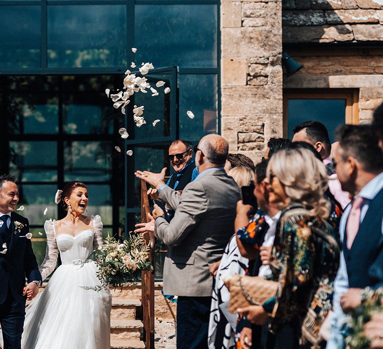 Bride and groom walk out to white petal confetti thrown over them after their rustic luxe wedding ceremony 