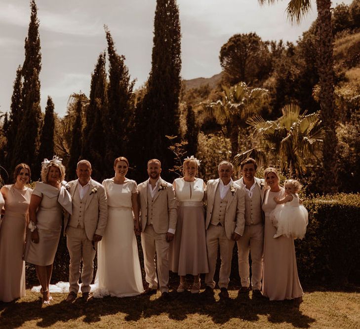 Bride & groom stand with their wedding party outdoors in front of tropical trees and hill backdrop 