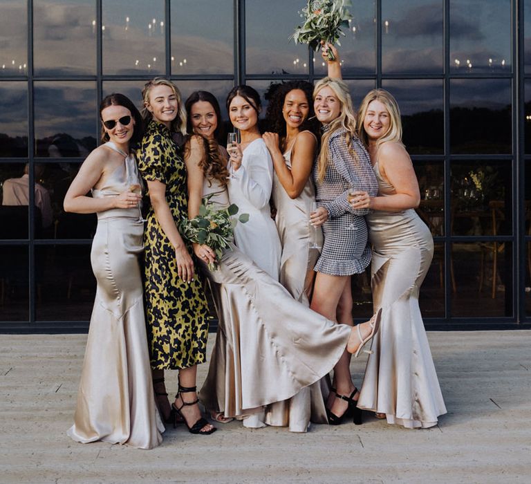 Bride poses with wedding guests and bridesmaids in front of tinted floor to ceiling windows 