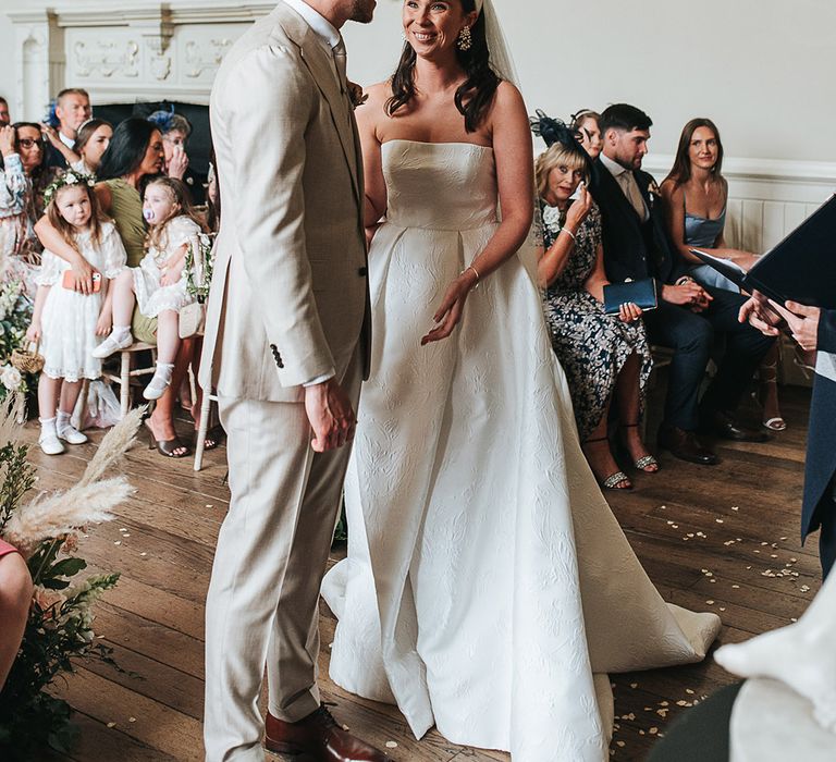 Groom in beige suit with bride in strapless pleated and brocade pattern Jesus Peiro wedding dress 