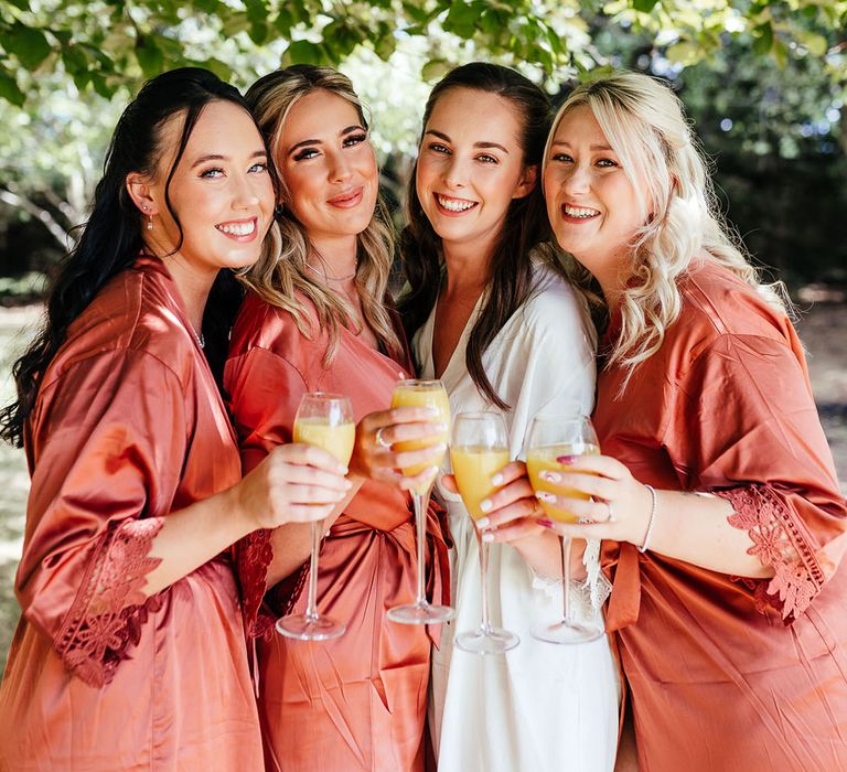 Bride with bridesmaids in orange satin robes as they get ready for the wedding 