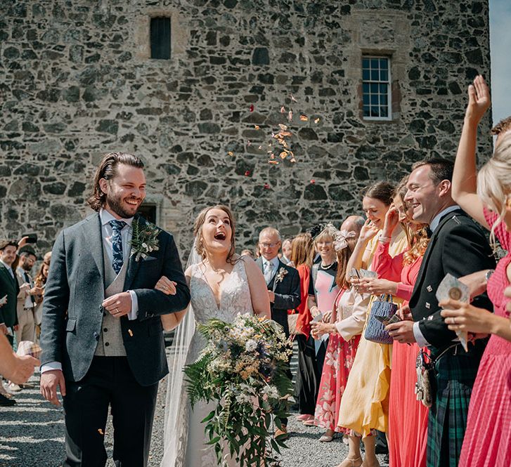 Bride holds oversized bouquet and walks through dried petal confetti being thrown above her