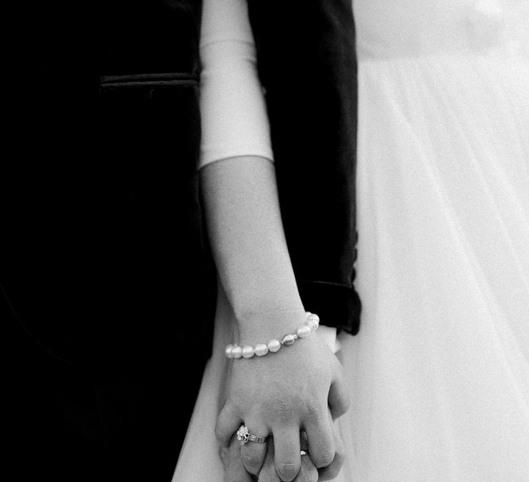 Bride holds grooms hand whilst wearing pearl bracelet and diamond ring 