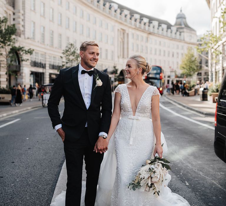 Groom wearing black tie walks through the city with his bride in Eva Lendal wedding dress with detachable skirt 