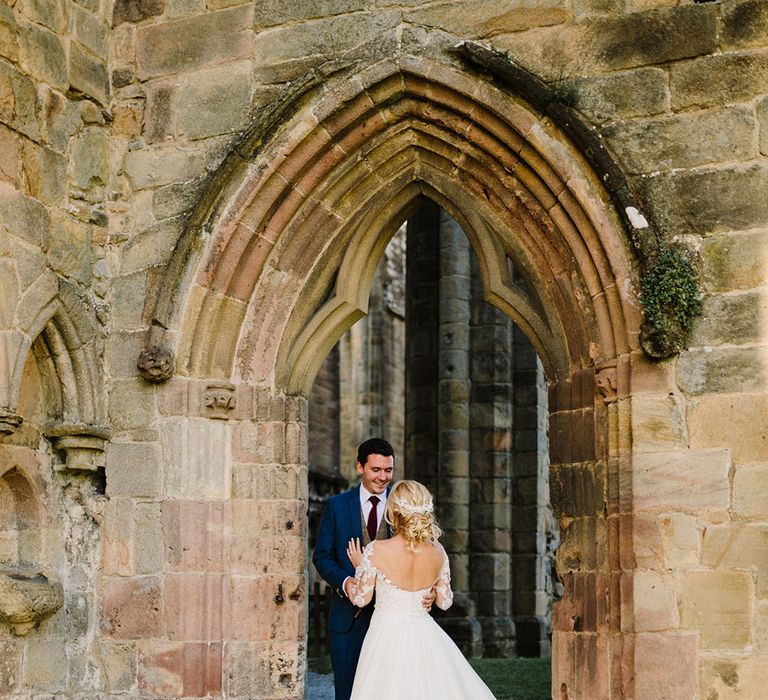 Bride wears her hair in intricate curled hair styling and Pronovias wedding dress as she looks toward her groom in three piece suit 