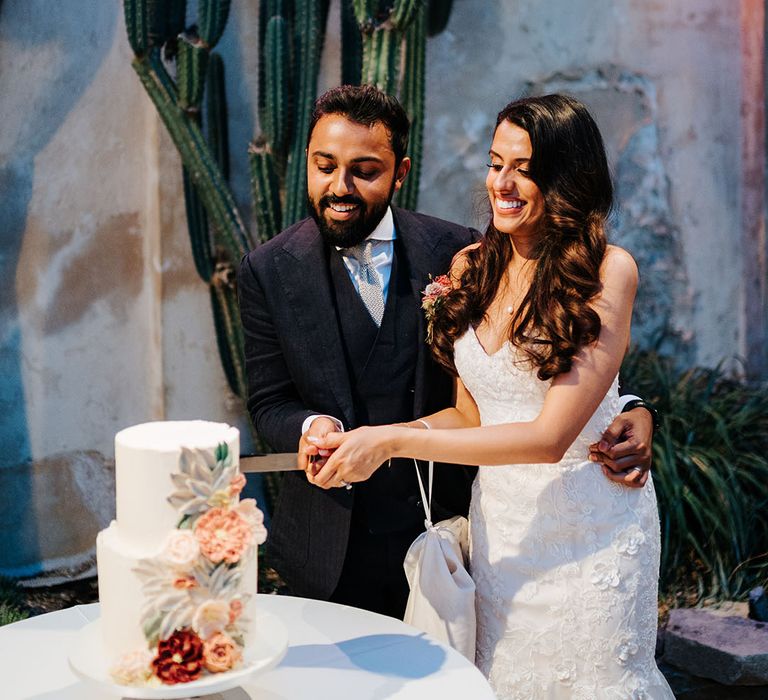 Bride & groom cut two-tier wedding cake complete with bright floral frosting