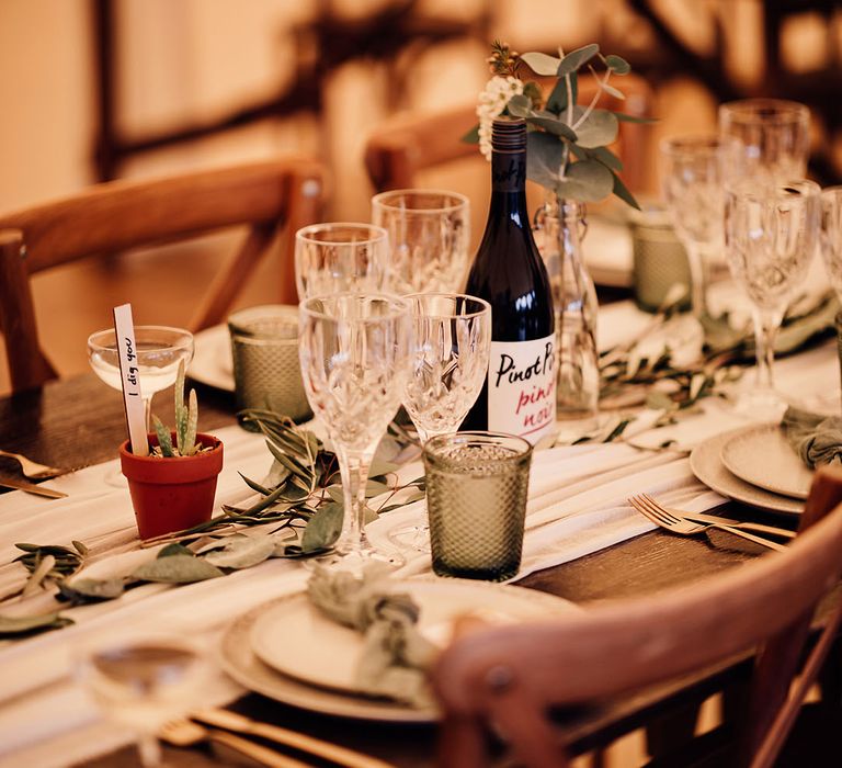 Green and white theme table setting with coloured glassware, leaves along the table runner, succulents and green napkins