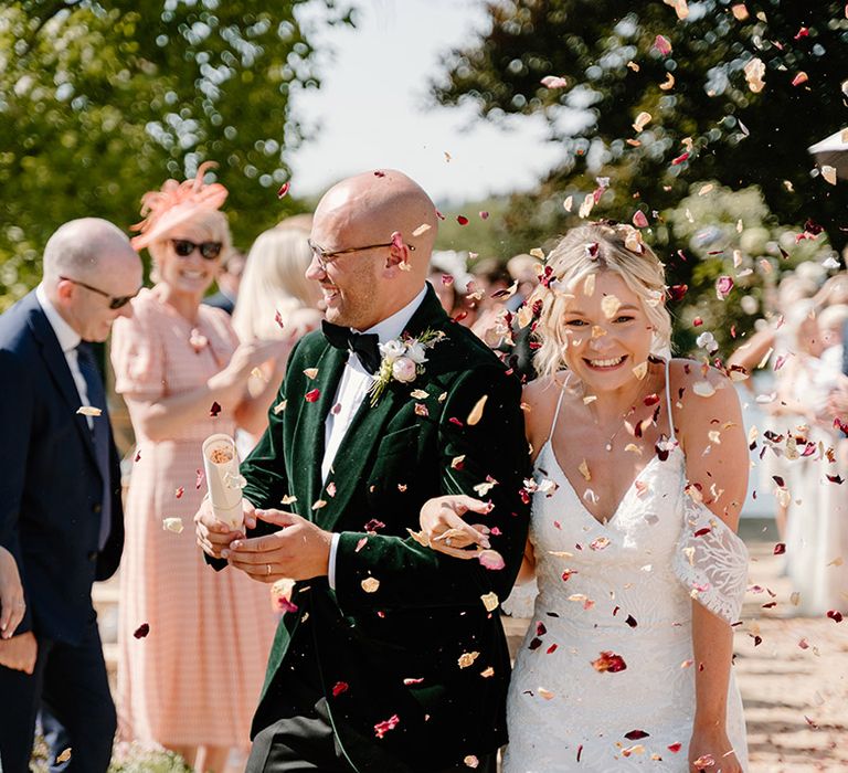 Groom wears green velvet black tie as confetti is thrown into the air by wedding guests 