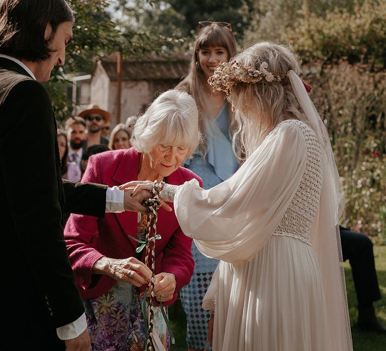 Bride wears puffed sleeves wedding dress as she holds her grooms hand during handfasting ceremony