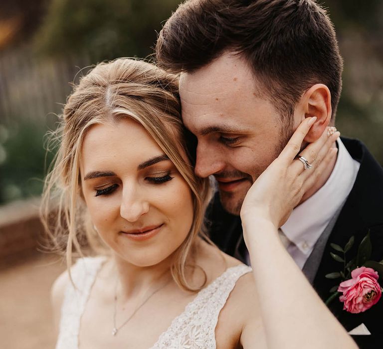 Bride in a v-neck lace and beaded wedding dress reaching back for the groom in a black suit and pink flower buttonhole 