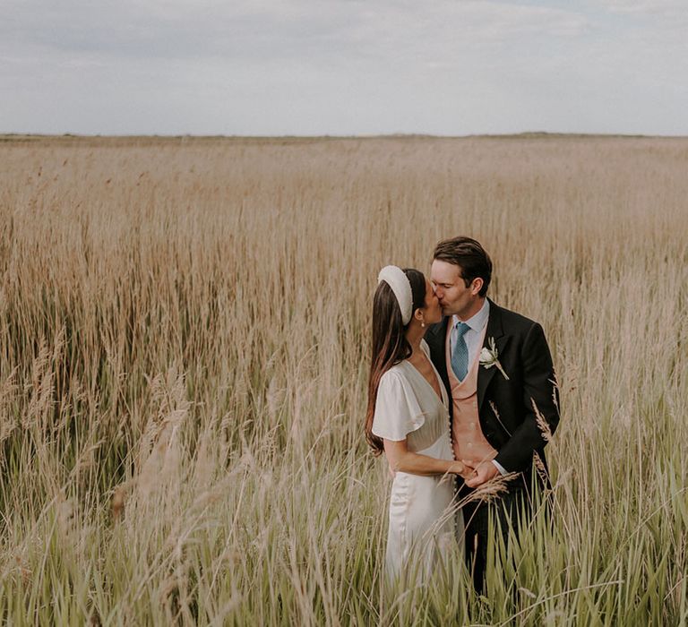 Bride in a satin wedding dress and chunky headband with the groom in a morning suit 