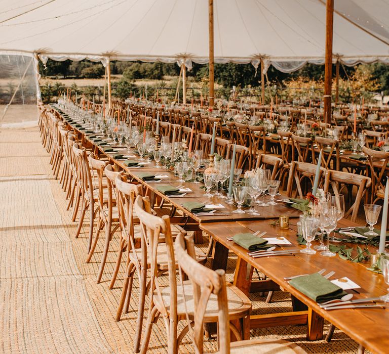 Wooden banquet tables complete with pastel green and orange candlesticks in brass antique styled holders beneath sailcloth tent