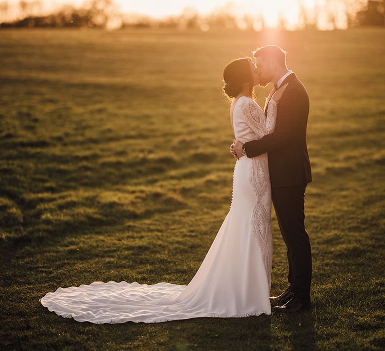 Bride in Atelier Pronovias wedding dress with a train shares a kiss with the groom in black tie during golden hour 