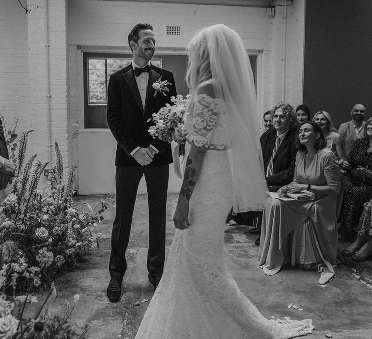 Bride in lace boho two piece with tattoos and short veil and groom in black tux with bow tie and boutonniere at Hackney Studios