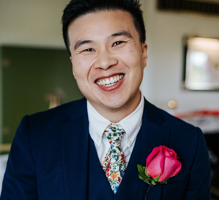 Groom wears three-piece blue suit complete with embroidered floral tie and pink rose buttonhole 