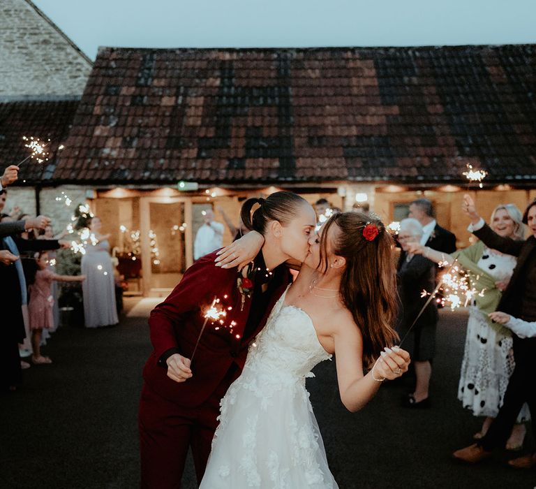 Brides kiss as they have a traditional sparkler send off from this rustic wedding at Kingscote Barn