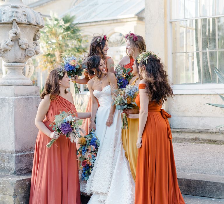 Bride in bespoke Emma Beaumont design wedding dress stands with her bridesmaids in ombre styled yellow and orange bridesmaid dresses