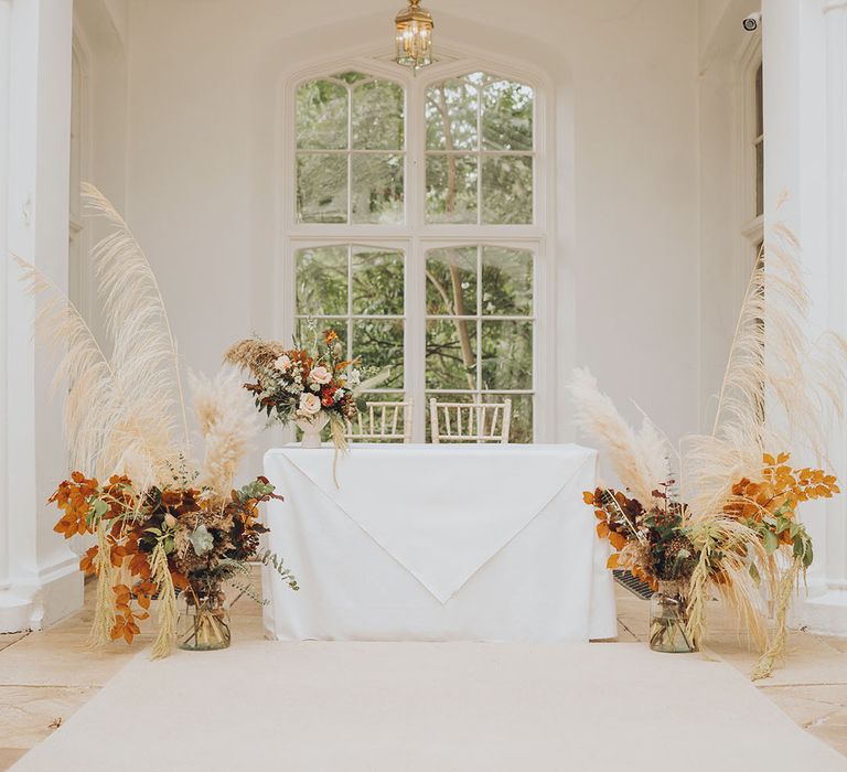 Pampas flower installations complete with dark foliage additions beside white table 