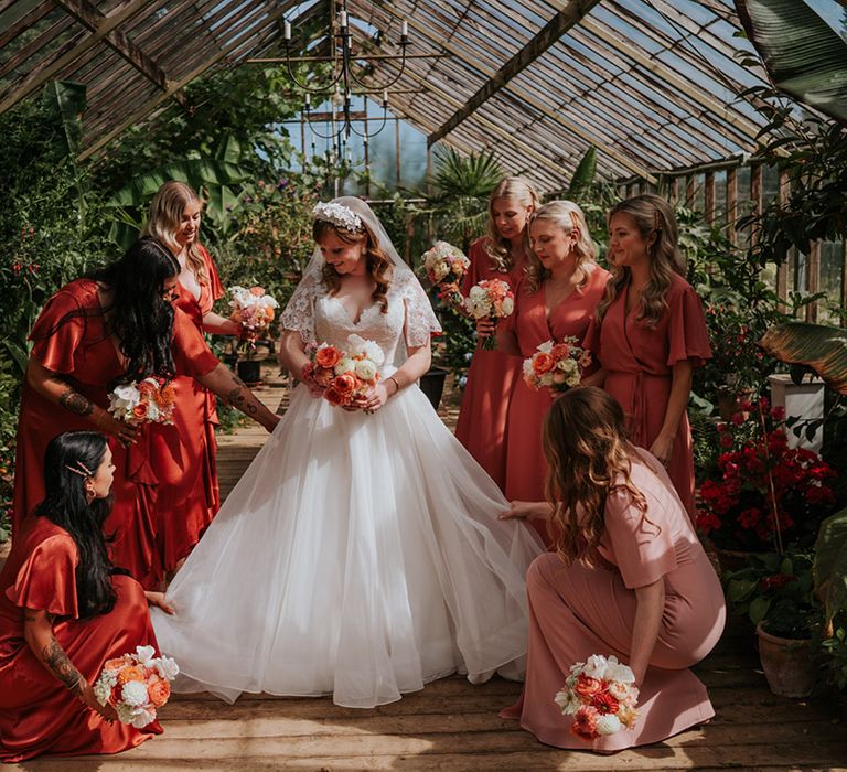 Bridesmaids in coral peach bridesmaid dresses stand with the bride in a greenhouse as they prepare for the wedding 