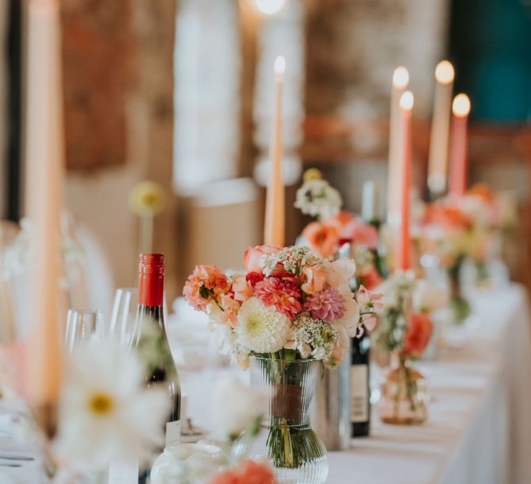 Coral, pink and white wedding flowers in vases decorate the wedding tables with coral and peach taper candles 