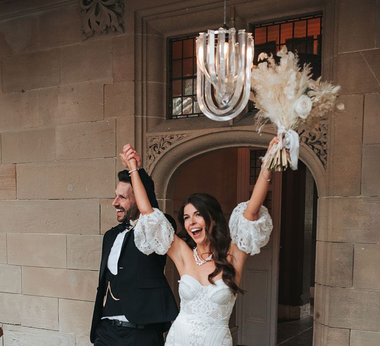 Groom in black tuxedo enters the wedding reception at Hampton Manor with the bride in detachable sleeve lace gown 