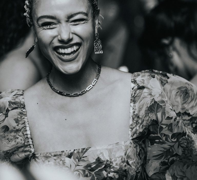 Wedding guest in floral dress smiles brightly in black & white image