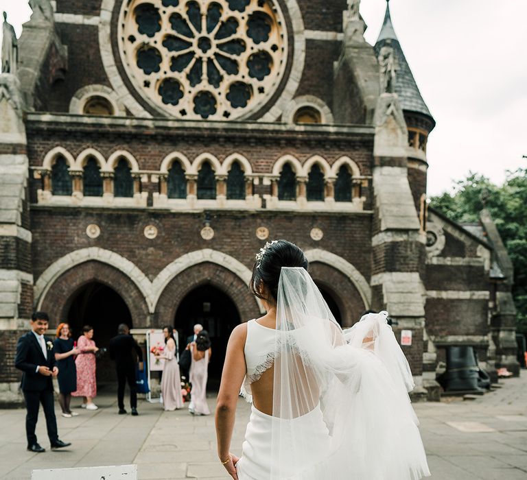 Bride wears fitted open back wedding dress with scallop lace edging and ruffled style veil 