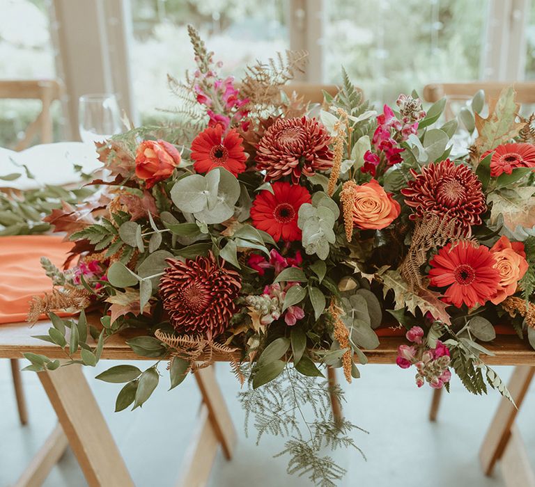 Autumnal wedding flower arrangement with red and orange flowers with roses, chrysanthemums, and foliage 