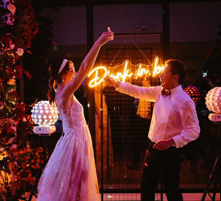 Bride & groom dance in front of custom neon wedding sign 