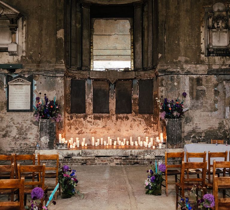 Asylum Chapel London wedding venue with pillar candles and purple hydrangeas, pink garden roses, purple orchids, lilac carnations, dried flowers and peacock blue feathers flower arrangements down the aisle and at the end of the aisle 