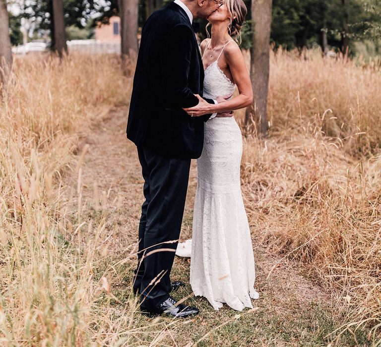 The groom in black tuxedo with the bride in a fitted lace wedding dress sharing a kiss as they pose for cute couple portraits 